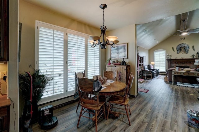 dining room featuring hardwood / wood-style flooring, vaulted ceiling, a brick fireplace, and ceiling fan with notable chandelier