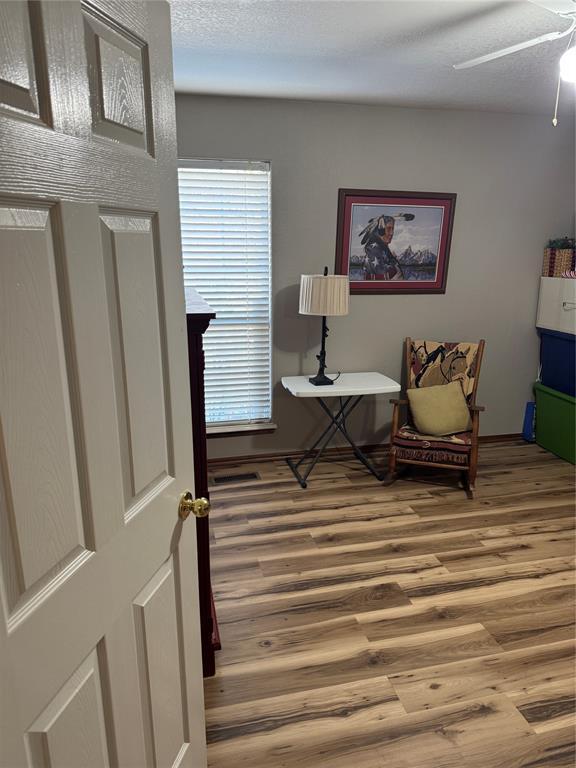 living area with hardwood / wood-style flooring, ceiling fan, and a textured ceiling