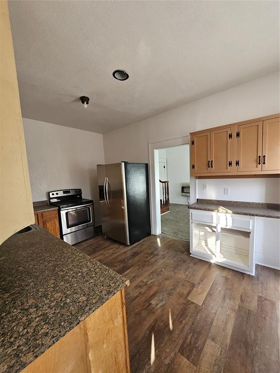 kitchen with dark stone counters, stainless steel appliances, dark hardwood / wood-style floors, and a textured ceiling