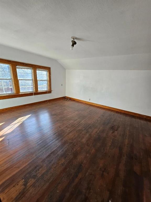 bonus room featuring dark wood-type flooring, a textured ceiling, and vaulted ceiling