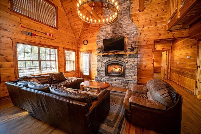 living room with wooden walls, high vaulted ceiling, wood-type flooring, a stone fireplace, and a chandelier