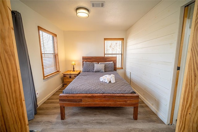 bedroom featuring multiple windows, dark hardwood / wood-style flooring, and wood walls