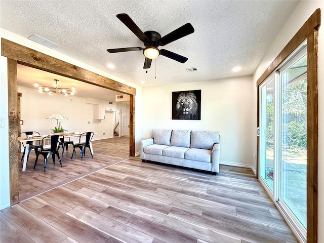 living room with wood-type flooring, ceiling fan with notable chandelier, and a textured ceiling