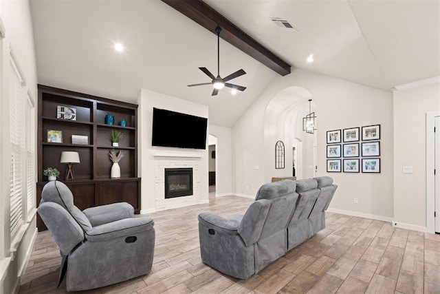 living room with arched walkways, vaulted ceiling with beams, visible vents, light wood-style floors, and a glass covered fireplace