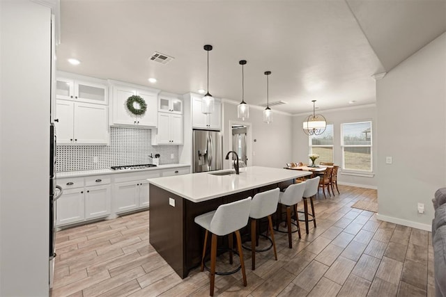 kitchen featuring visible vents, light countertops, an island with sink, stainless steel fridge, and glass insert cabinets