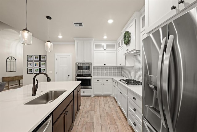 kitchen with appliances with stainless steel finishes, light countertops, glass insert cabinets, and a sink