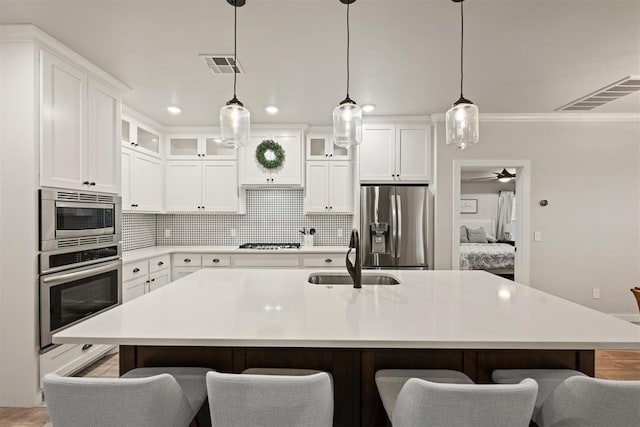 kitchen featuring appliances with stainless steel finishes, glass insert cabinets, an island with sink, and a sink