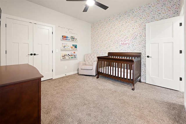 bedroom featuring light carpet, a nursery area, a ceiling fan, and wallpapered walls