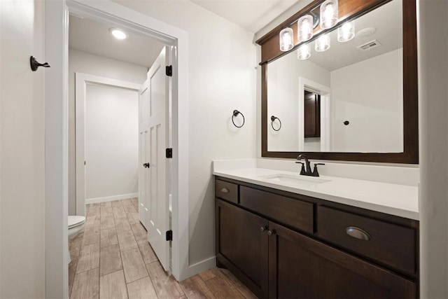 bathroom featuring baseboards, visible vents, toilet, vanity, and wood finish floors