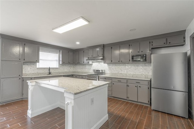 kitchen with sink, a center island, appliances with stainless steel finishes, light stone countertops, and backsplash