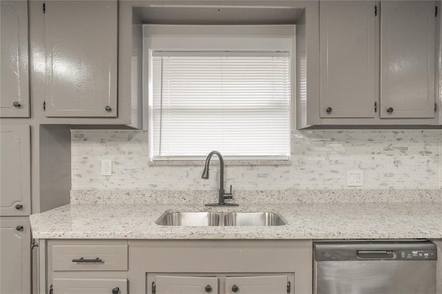 kitchen featuring sink, gray cabinetry, light stone counters, stainless steel dishwasher, and backsplash