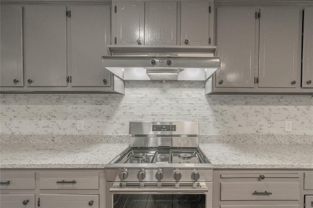 kitchen featuring gray cabinets, backsplash, range hood, stainless steel gas range oven, and light stone countertops