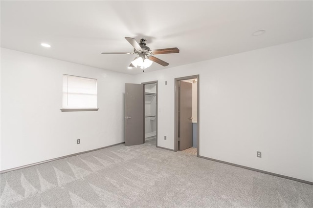 unfurnished bedroom with a walk in closet, light carpet, and ceiling fan