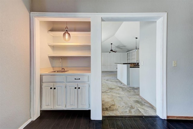 hallway featuring wood finished floors, a sink, lofted ceiling, and baseboards