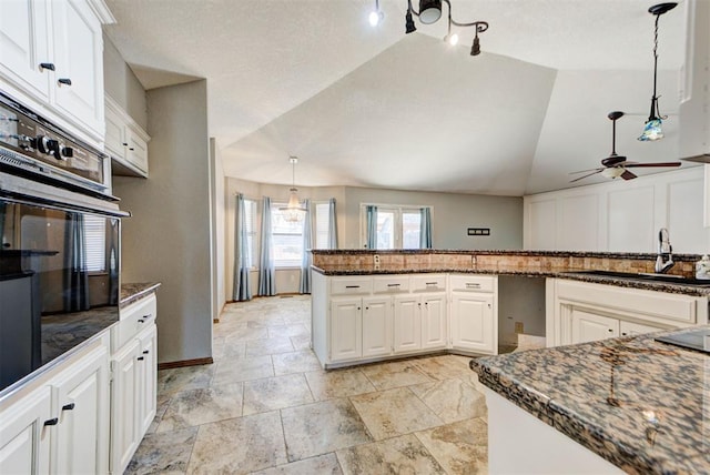 kitchen featuring hanging light fixtures, oven, a sink, ceiling fan with notable chandelier, and lofted ceiling
