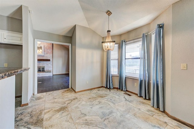 unfurnished dining area with visible vents, baseboards, a chandelier, and a brick fireplace