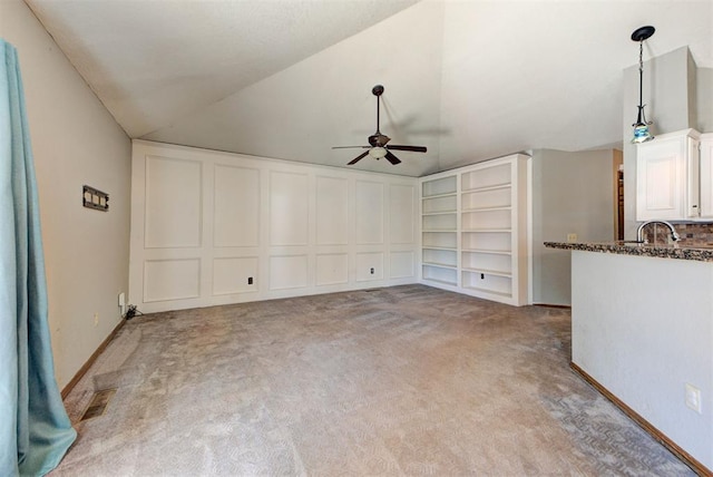unfurnished living room featuring vaulted ceiling, ceiling fan, built in shelves, light colored carpet, and a sink