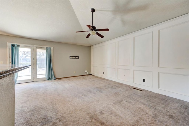 unfurnished living room featuring visible vents, a decorative wall, ceiling fan, vaulted ceiling, and light colored carpet