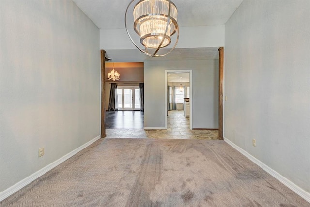 carpeted spare room with baseboards and a chandelier