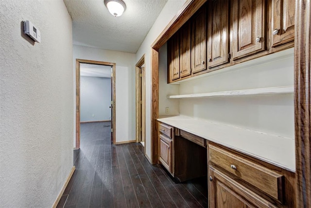 hallway featuring a textured ceiling, a textured wall, baseboards, and dark wood finished floors