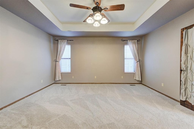 spare room featuring a tray ceiling, baseboards, and carpet flooring