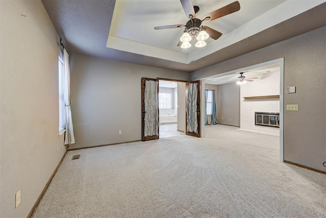 carpeted empty room with baseboards, a brick fireplace, a tray ceiling, visible vents, and ceiling fan