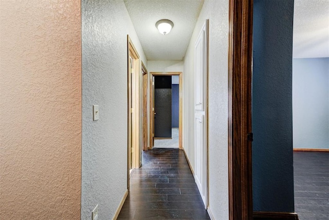 hallway featuring a textured wall, baseboards, a textured ceiling, and dark wood finished floors