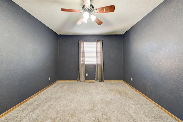 carpeted spare room with a textured wall, baseboards, and a ceiling fan