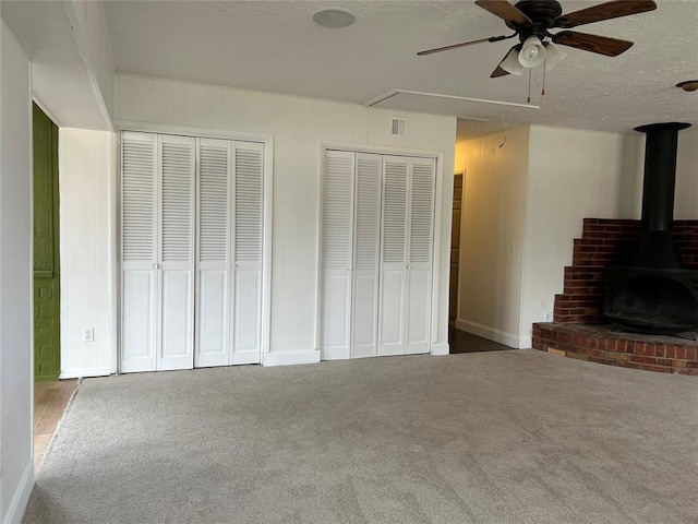 unfurnished living room with ceiling fan, carpet floors, a textured ceiling, and a wood stove