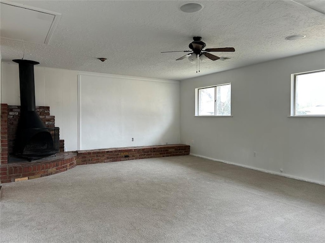 unfurnished living room with ceiling fan, a wood stove, a textured ceiling, and carpet flooring