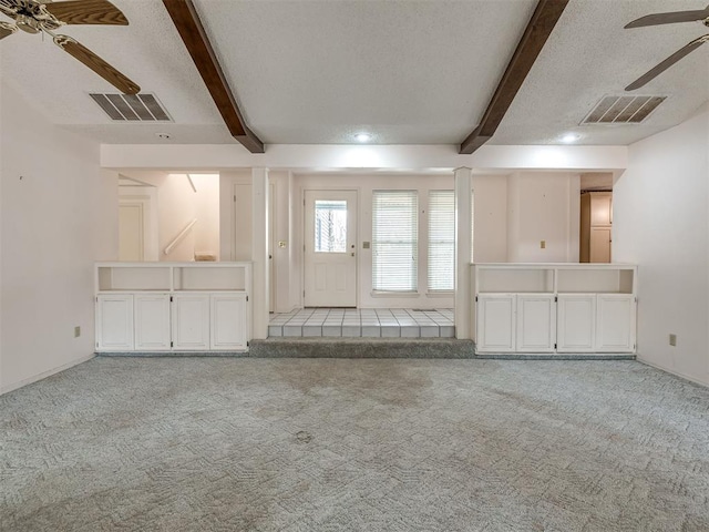 unfurnished living room with ceiling fan, a textured ceiling, light colored carpet, and beamed ceiling