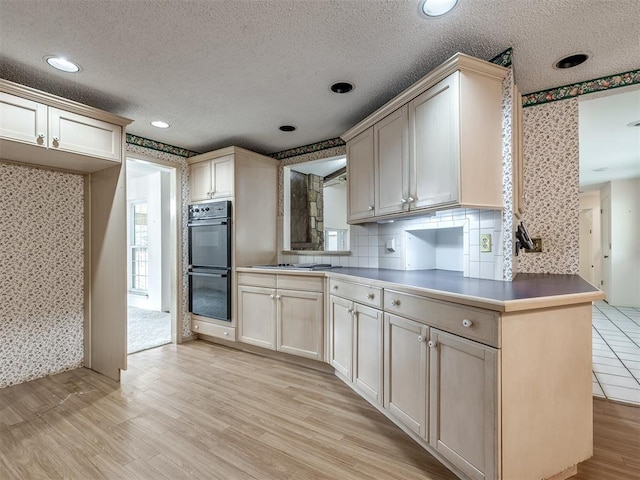 kitchen featuring black double oven, kitchen peninsula, a textured ceiling, and light wood-type flooring