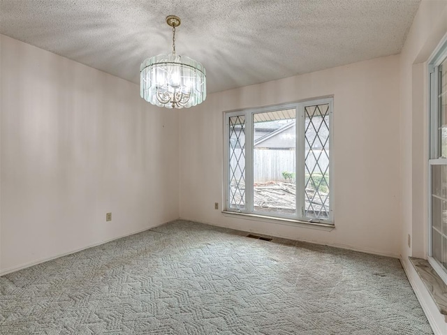 spare room featuring light colored carpet, a textured ceiling, and a notable chandelier