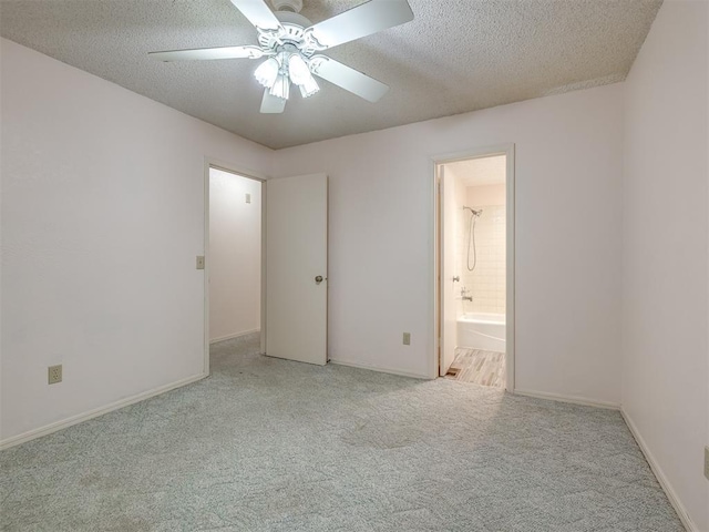 unfurnished bedroom featuring light carpet, ceiling fan, ensuite bath, and a textured ceiling