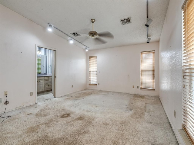 carpeted empty room featuring ceiling fan, track lighting, and a textured ceiling