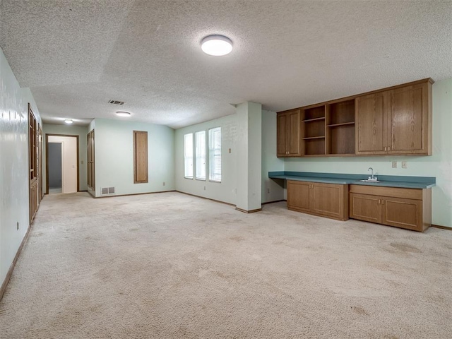 kitchen featuring built in desk, sink, light carpet, and a textured ceiling