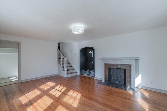 unfurnished living room featuring a tiled fireplace, hardwood / wood-style flooring, and a textured ceiling