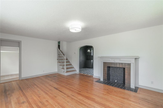 3125 NW 24th St, Oklahoma City, OK 73107 - unfurnished living room featuring arched walkways, wood finished floors, a fireplace, stairs, and a textured ceiling