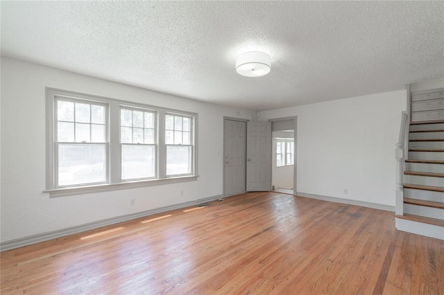3125 NW 24th St, Oklahoma City, OK 73107 - unfurnished living room featuring a textured ceiling, light wood finished floors, baseboards, and stairs