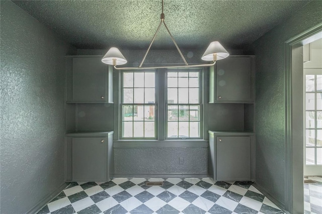 3125 NW 24th St, Oklahoma City, OK 73107 - unfurnished dining area featuring a textured wall, healthy amount of natural light, tile patterned floors, a textured ceiling, and baseboards