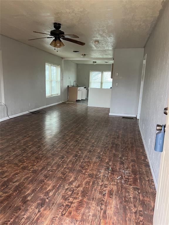 unfurnished living room with dark wood-type flooring, ceiling fan, and a textured ceiling