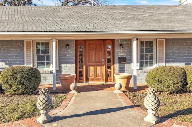 property entrance featuring brick siding, roof with shingles, and a porch