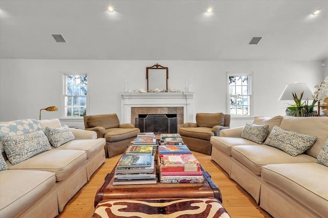 living room with light wood-type flooring, visible vents, a wealth of natural light, and a tile fireplace