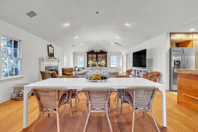 kitchen with a premium fireplace, light wood-style floors, vaulted ceiling, light countertops, and stainless steel refrigerator with ice dispenser