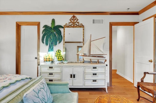 bedroom with light wood finished floors, baseboards, visible vents, and ornamental molding