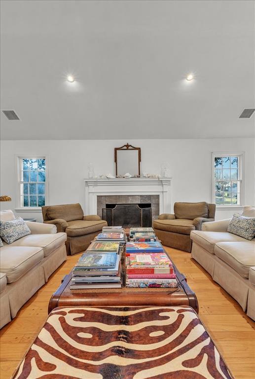 living area with a tile fireplace, visible vents, vaulted ceiling, and light wood-style flooring