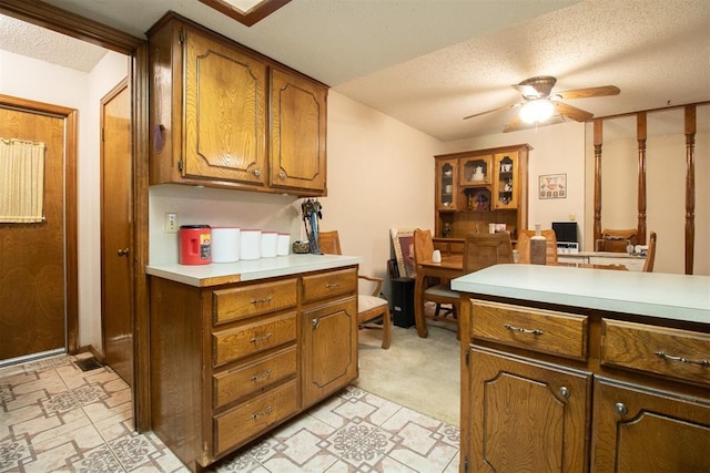 kitchen with a textured ceiling, light countertops, a ceiling fan, and brown cabinets