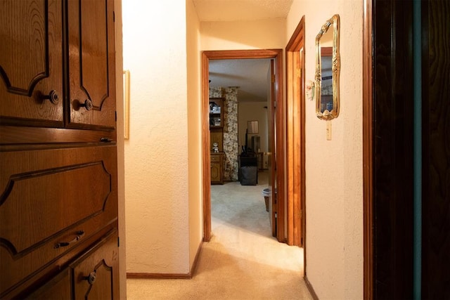 hall featuring baseboards, a textured wall, and light colored carpet