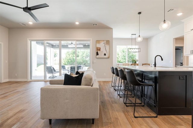 kitchen featuring decorative light fixtures, a breakfast bar area, white cabinets, a kitchen island with sink, and light wood-type flooring