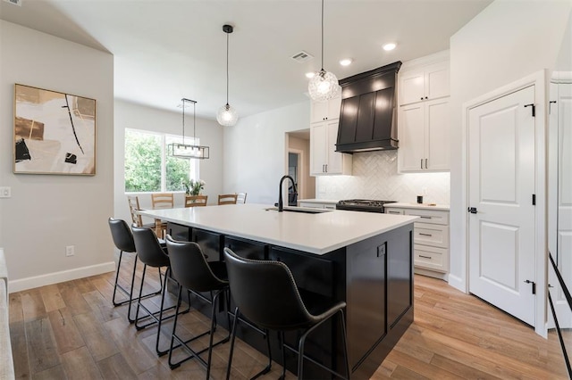 kitchen with white cabinetry, sink, a kitchen island with sink, and custom range hood